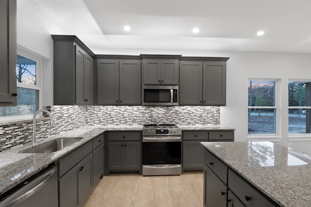 kitchen featuring backsplash, light stone counters, appliances with stainless steel finishes, and sink