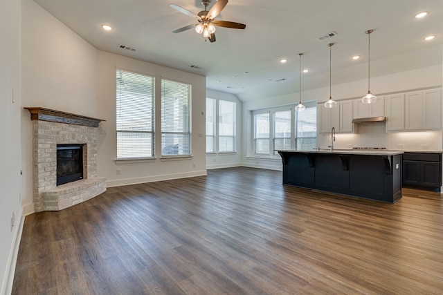 kitchen with pendant lighting, an island with sink, dark hardwood / wood-style floors, white cabinetry, and a fireplace