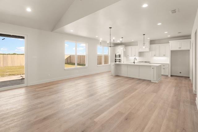 kitchen with sink, decorative light fixtures, light hardwood / wood-style flooring, a center island with sink, and white cabinets