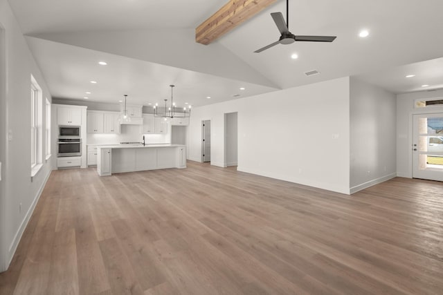 unfurnished living room with ceiling fan with notable chandelier, lofted ceiling with beams, and light wood-type flooring