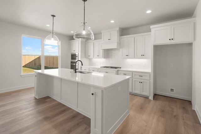 kitchen with white cabinetry, sink, pendant lighting, and an island with sink