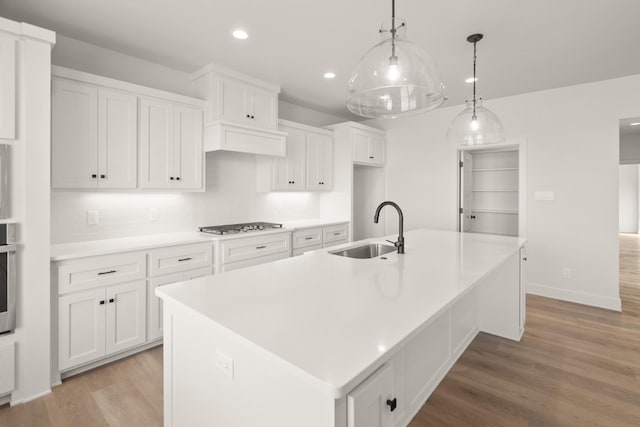 kitchen featuring a kitchen island with sink, sink, hanging light fixtures, and white cabinets