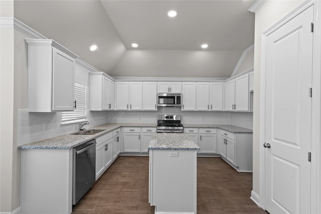 kitchen with light stone countertops, stainless steel appliances, vaulted ceiling, and a center island