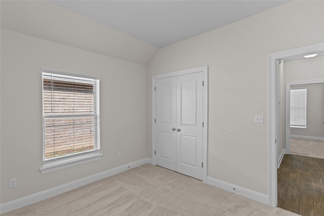 unfurnished bedroom with light wood-type flooring, lofted ceiling, and a closet