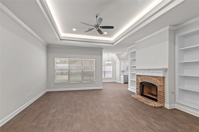 unfurnished living room with built in features, ornamental molding, dark hardwood / wood-style floors, a fireplace, and ceiling fan with notable chandelier