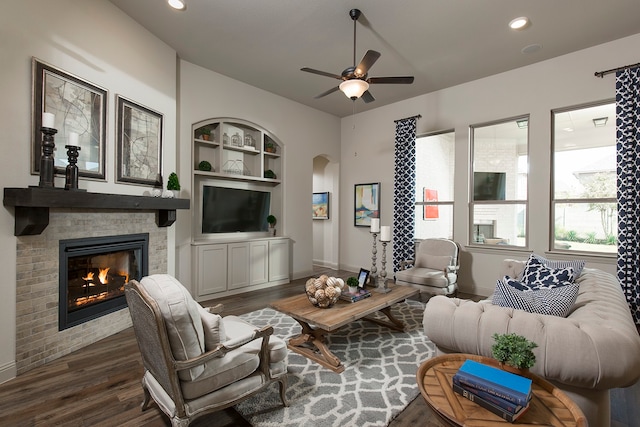 living room with built in shelves, a fireplace, dark hardwood / wood-style flooring, and ceiling fan