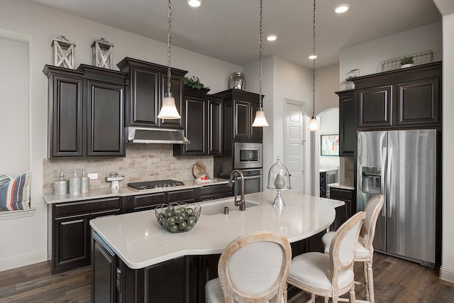 kitchen featuring pendant lighting, dark hardwood / wood-style floors, a kitchen island with sink, tasteful backsplash, and appliances with stainless steel finishes