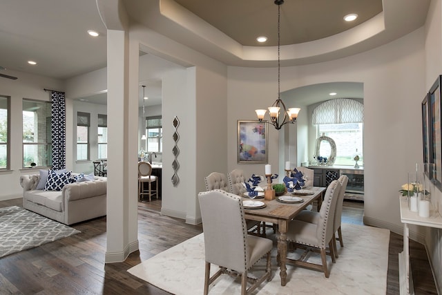 dining area with an inviting chandelier, a raised ceiling, and hardwood / wood-style floors