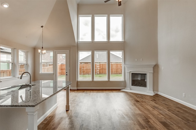 unfurnished living room featuring high vaulted ceiling, light hardwood / wood-style floors, ceiling fan with notable chandelier, and sink