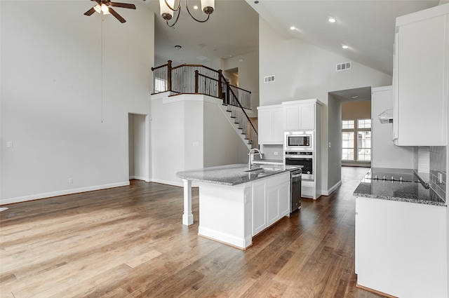 kitchen featuring appliances with stainless steel finishes, a kitchen island with sink, high vaulted ceiling, and white cabinetry