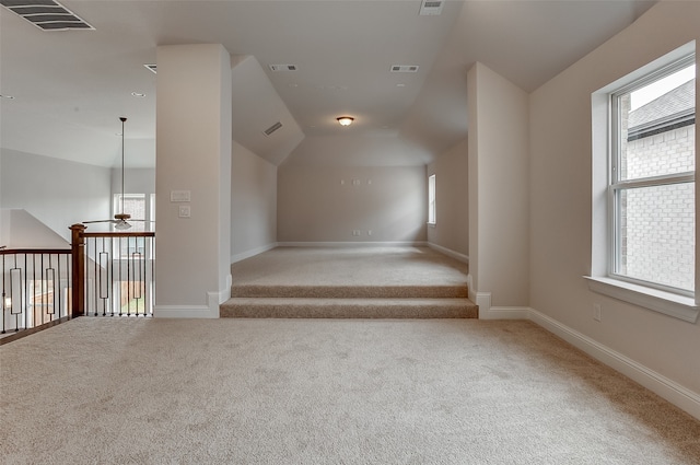 additional living space featuring a wealth of natural light, vaulted ceiling, ceiling fan, and light colored carpet