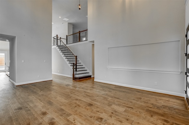 unfurnished living room with wood-type flooring and a towering ceiling