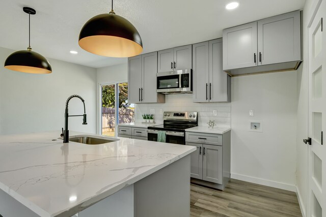 kitchen featuring light wood-type flooring, sink, hanging light fixtures, appliances with stainless steel finishes, and light stone countertops