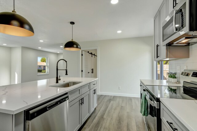 kitchen with appliances with stainless steel finishes, light hardwood / wood-style floors, sink, and decorative light fixtures