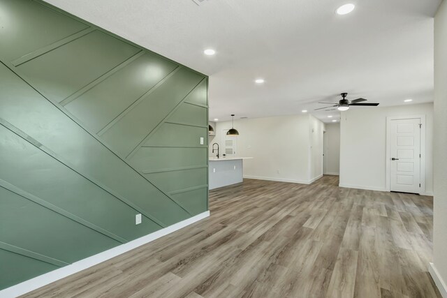 unfurnished living room featuring light hardwood / wood-style floors, ceiling fan, and sink