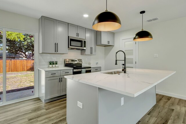 kitchen featuring hanging light fixtures, sink, a kitchen island with sink, appliances with stainless steel finishes, and light stone countertops