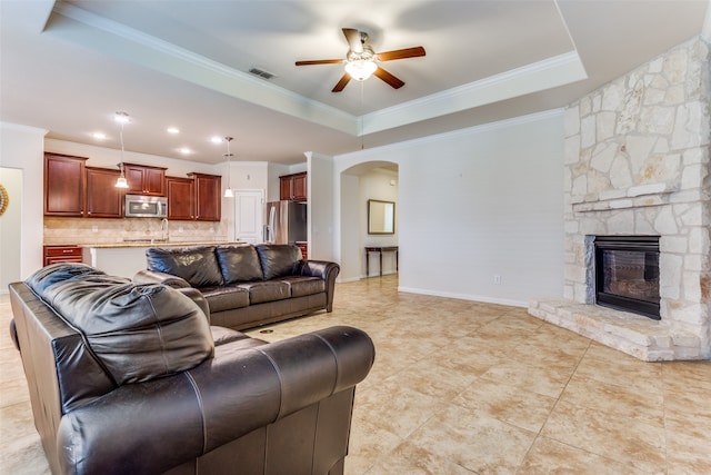 living room with light tile patterned floors, ceiling fan, a raised ceiling, crown molding, and a fireplace