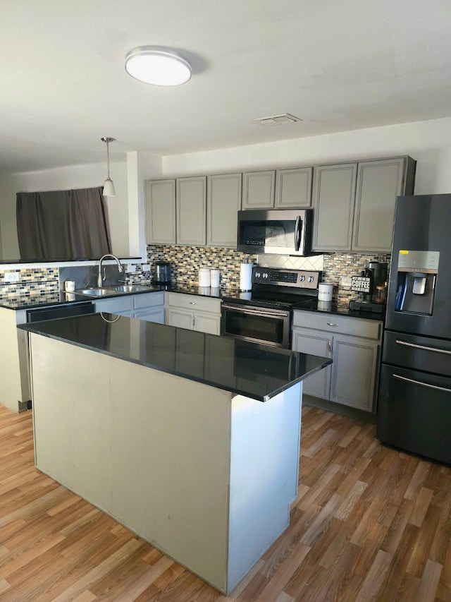 kitchen featuring backsplash, appliances with stainless steel finishes, hanging light fixtures, and hardwood / wood-style floors