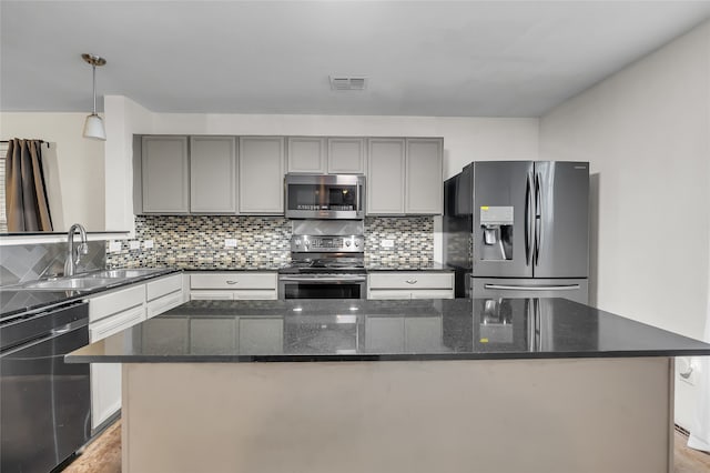 kitchen with a kitchen island, dark stone counters, stainless steel appliances, sink, and decorative light fixtures