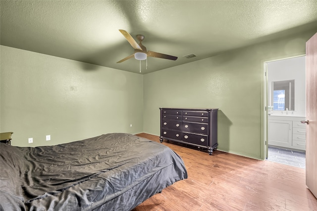 bedroom featuring light hardwood / wood-style floors, a textured ceiling, connected bathroom, and ceiling fan