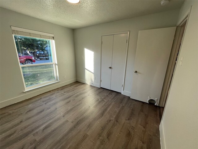 unfurnished bedroom featuring a textured ceiling, dark hardwood / wood-style flooring, and a closet