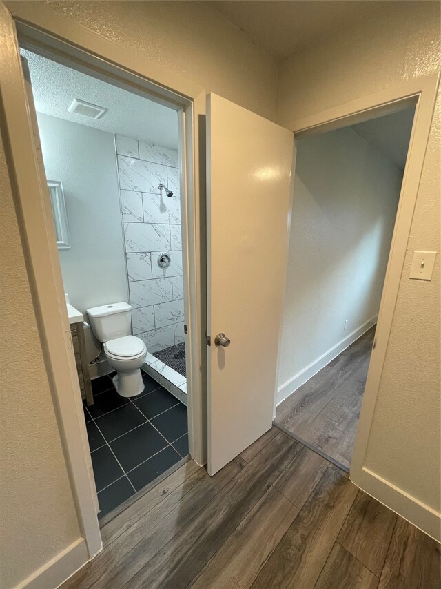 bathroom with a textured ceiling, hardwood / wood-style flooring, tiled shower, vanity, and toilet