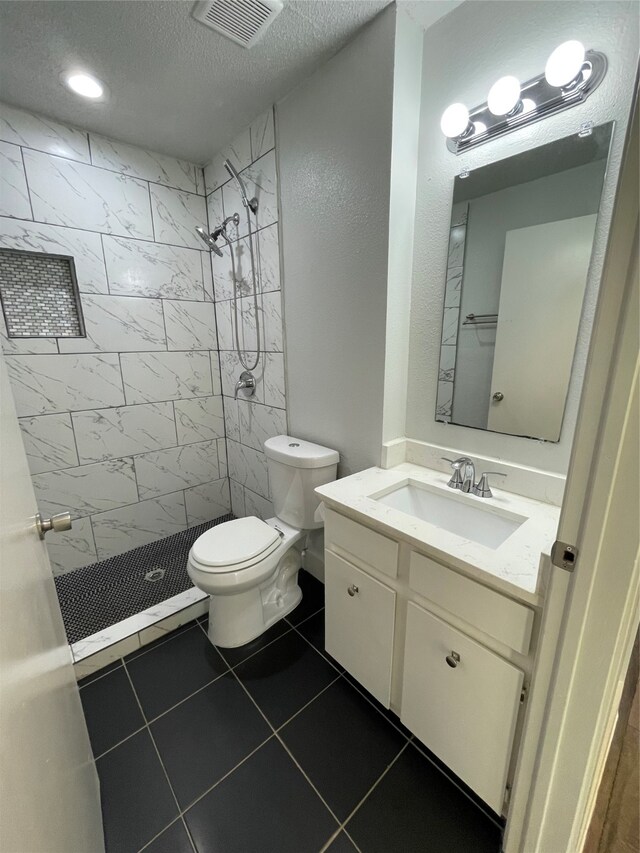 bathroom with tiled shower, vanity, toilet, and tile patterned flooring