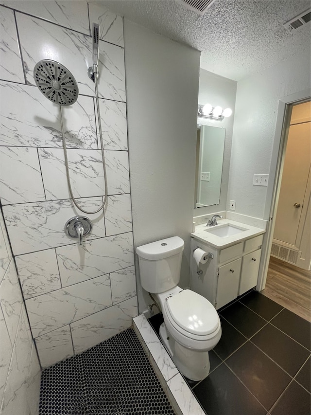 bathroom featuring vanity, tiled shower, a textured ceiling, tile patterned floors, and toilet