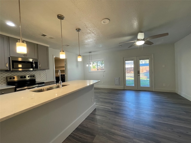 kitchen featuring backsplash, dark wood-type flooring, gray cabinets, stainless steel appliances, and light stone countertops