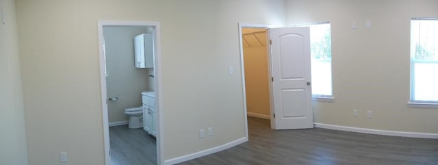 unfurnished bedroom featuring ensuite bath, dark wood-type flooring, and a walk in closet