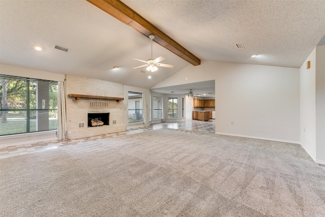 unfurnished living room with beamed ceiling, a brick fireplace, light colored carpet, a textured ceiling, and ceiling fan