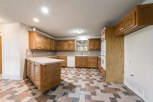 kitchen featuring white appliances, a textured ceiling, sink, and kitchen peninsula