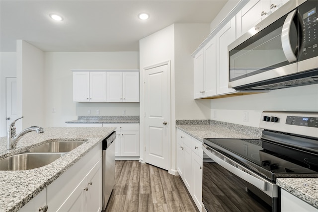 kitchen with appliances with stainless steel finishes, white cabinets, light stone countertops, hardwood / wood-style floors, and sink