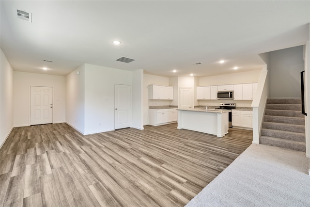 kitchen with white cabinets, sink, a kitchen island with sink, stainless steel appliances, and light hardwood / wood-style floors