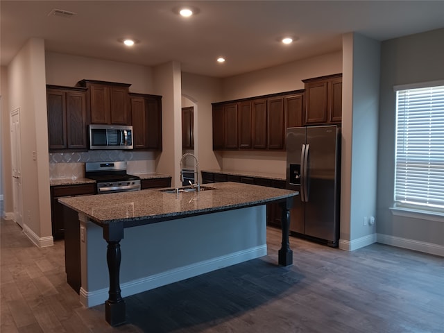 kitchen featuring light wood-type flooring, dark stone countertops, appliances with stainless steel finishes, a kitchen bar, and a center island with sink