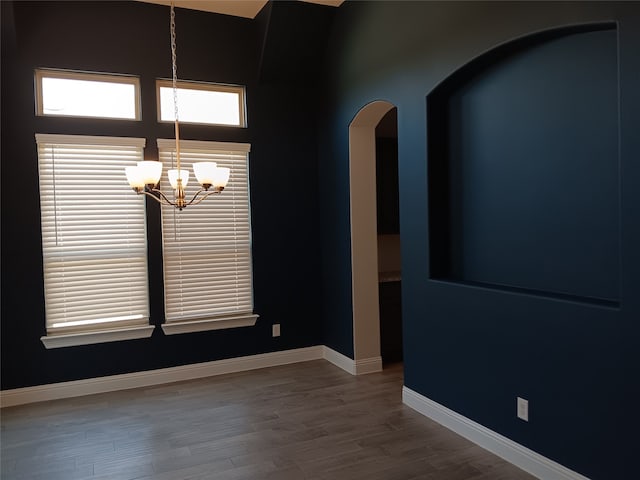 empty room with a high ceiling, hardwood / wood-style floors, and a chandelier