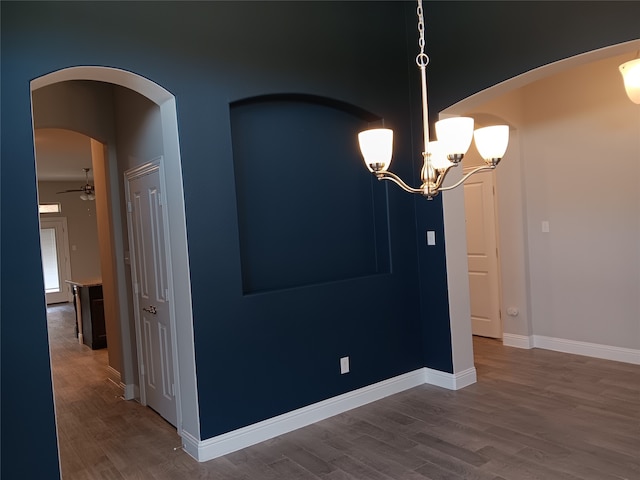 unfurnished dining area featuring ceiling fan with notable chandelier and wood-type flooring