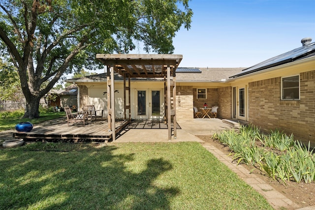 rear view of property with solar panels, a wooden deck, a lawn, and a patio area