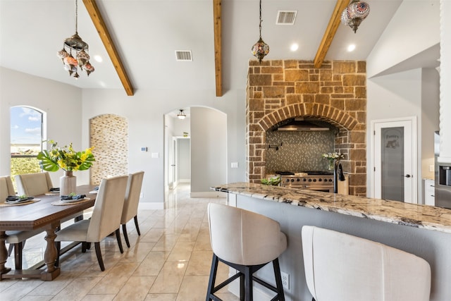 kitchen with decorative light fixtures, beam ceiling, high end stainless steel range oven, and light stone counters