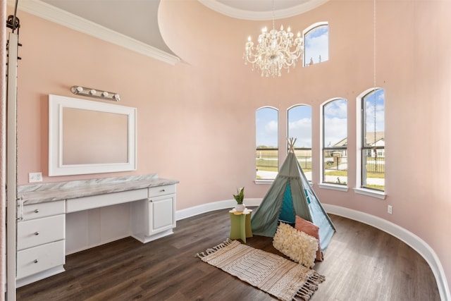 recreation room featuring a high ceiling, built in desk, dark hardwood / wood-style floors, and ornamental molding