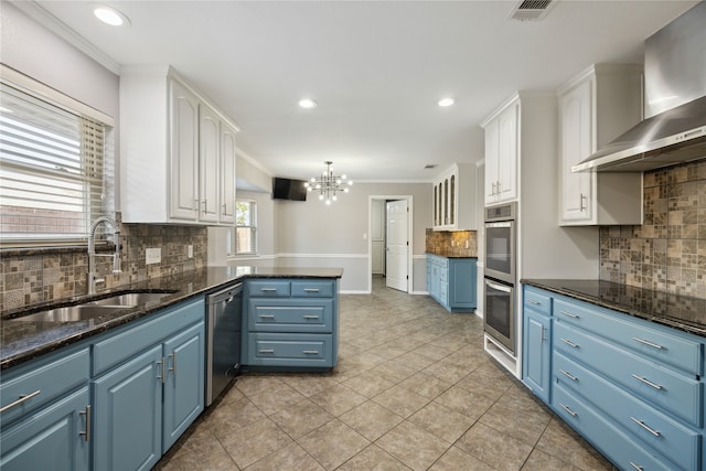 kitchen with appliances with stainless steel finishes, wall chimney exhaust hood, blue cabinets, sink, and white cabinetry