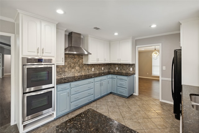 kitchen featuring ornamental molding, black appliances, blue cabinetry, wall chimney range hood, and white cabinetry