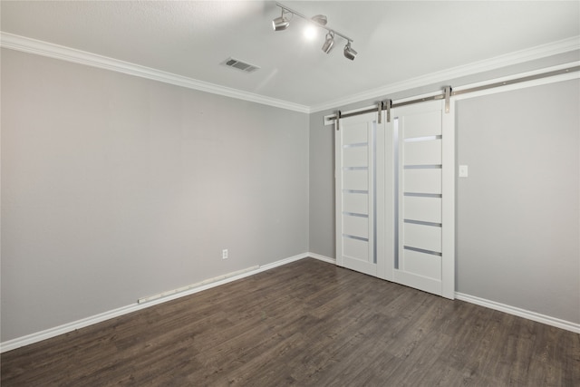 unfurnished bedroom featuring a barn door, crown molding, rail lighting, and dark hardwood / wood-style floors