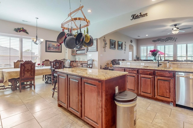 kitchen with a center island, sink, decorative light fixtures, light stone countertops, and stainless steel dishwasher