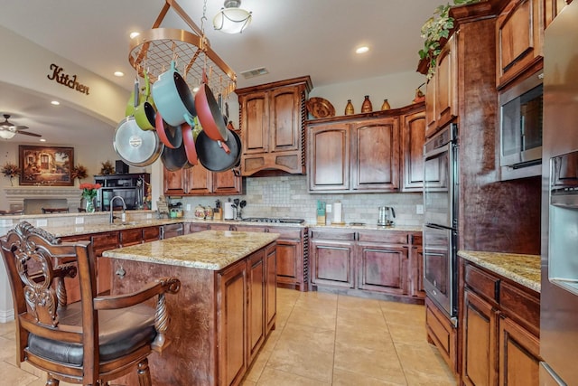 kitchen featuring ceiling fan, stainless steel appliances, a center island, light stone countertops, and decorative backsplash