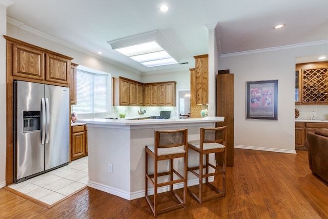 kitchen with a breakfast bar, kitchen peninsula, light hardwood / wood-style flooring, ornamental molding, and stainless steel fridge with ice dispenser