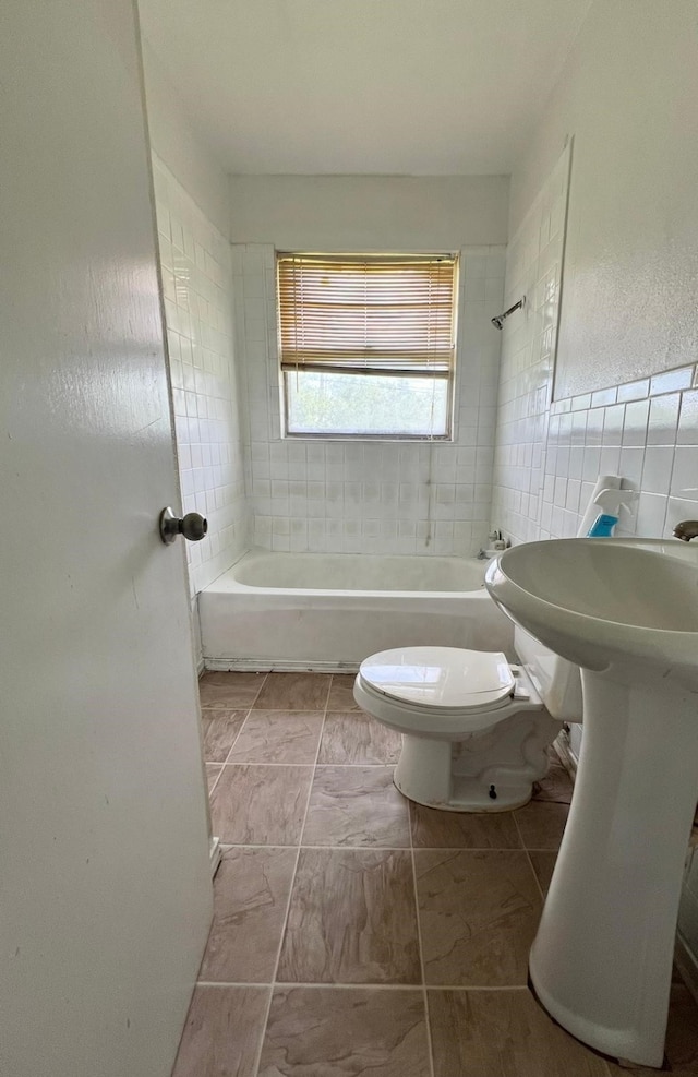 bathroom with tile walls, tiled shower / bath combo, tile patterned floors, and toilet