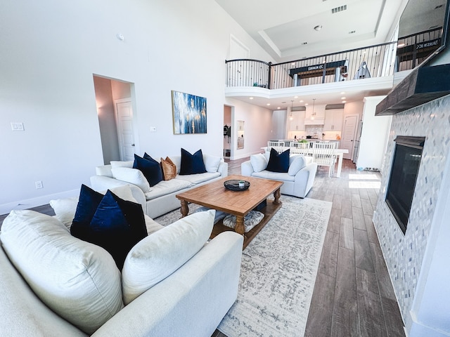 living room featuring a stone fireplace, a high ceiling, and hardwood / wood-style floors