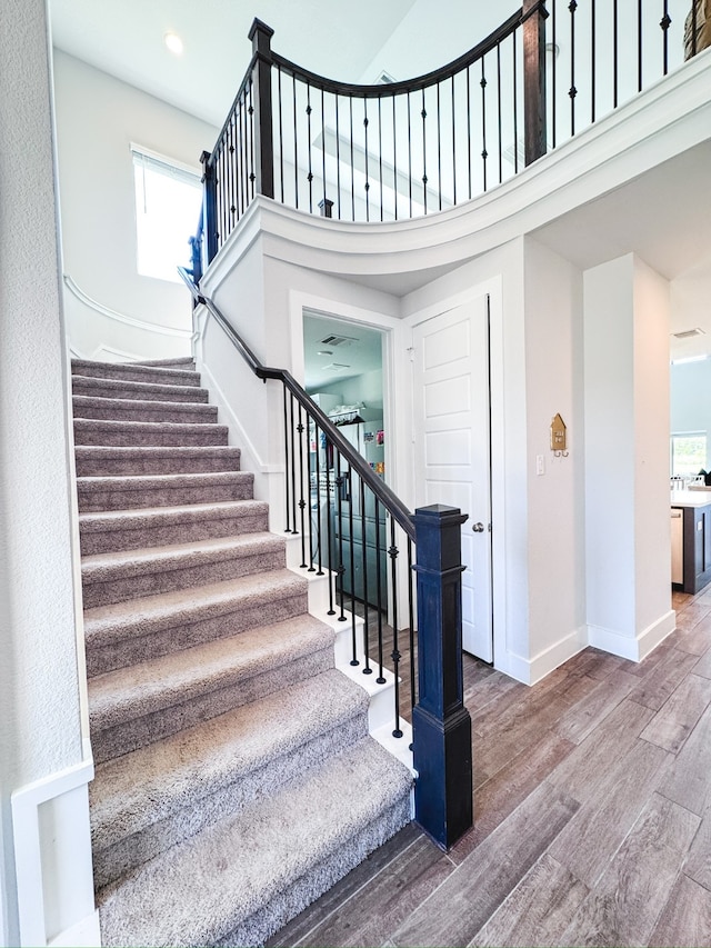 stairway with hardwood / wood-style floors, a towering ceiling, and plenty of natural light