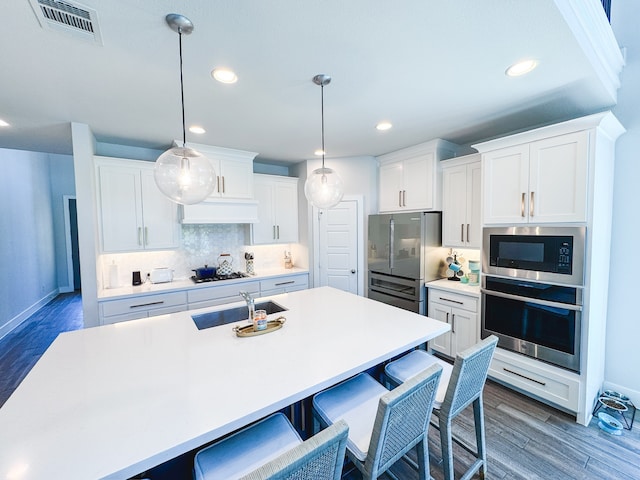 kitchen with appliances with stainless steel finishes, white cabinetry, dark wood-type flooring, pendant lighting, and sink